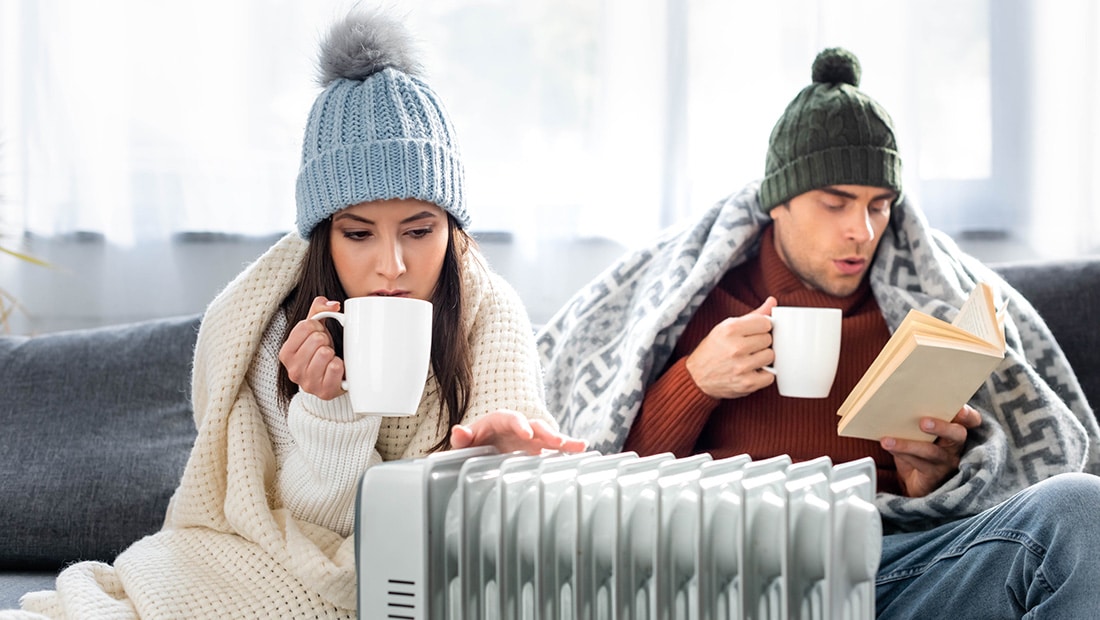Couple bundled up in front of a portable heater in their living room