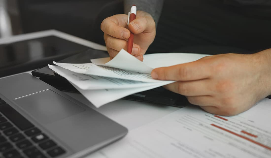 Man with laptop open and pen in hand reviewing utility bills
